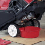 Draining oil from Toro engine into red bucket in garage