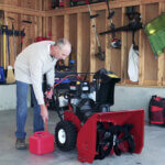 Man in garage removing fuel Toro product with tube