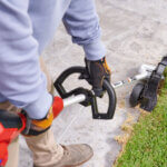 Man uses a handheld electric edger for edging the lawn along a stone path