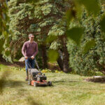 Man looks across lawn from behind walk behind lawn mower.