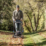 Man mows leaf-covered lawn with a walk behind mower